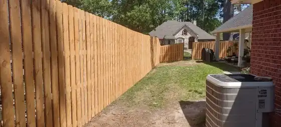 Stained board-on-board privacy fence running the length of a backyard beside an AC unit
