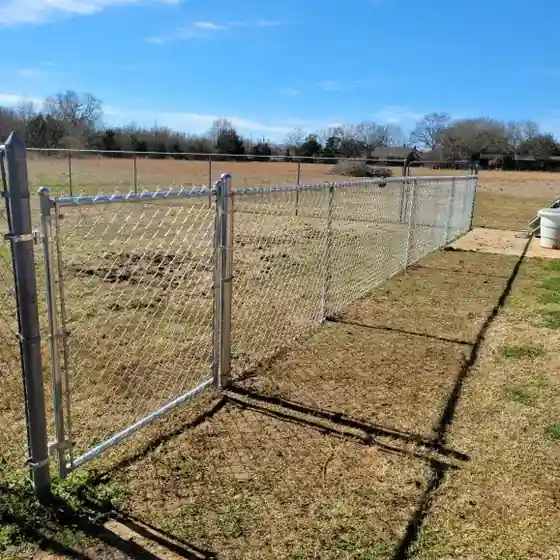 Galvanized chain link fence and walk gate running along an open pasture