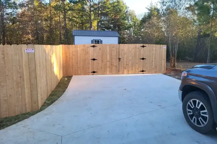 New cedar privacy fence and double drive gate at a concrete driveway, with the red CWG sign on the fence