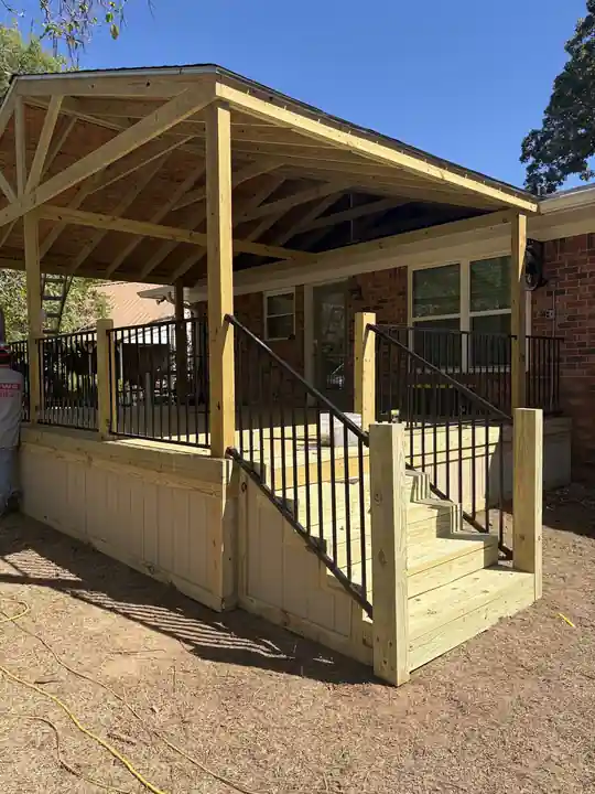 Covered porch deck with a gable roof, black iron balusters and wide stairs on a brick home