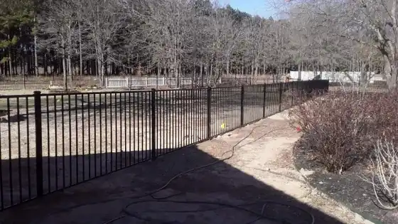 Long black ornamental iron fence run along the edge of a field with bare winter trees