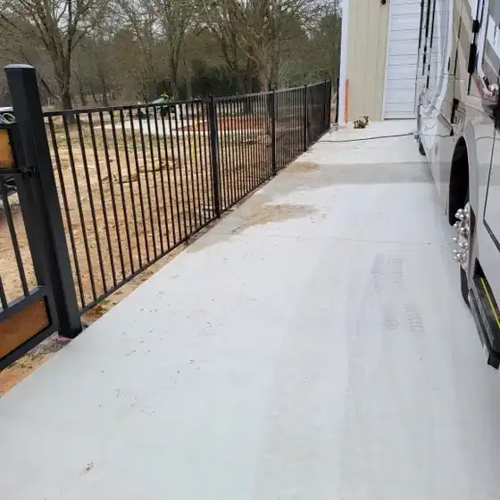 Black ornamental iron fence running beside a concrete drive