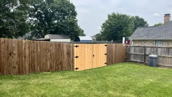 A new pine privacy fence with a double gate between older fence runs, over a green lawn