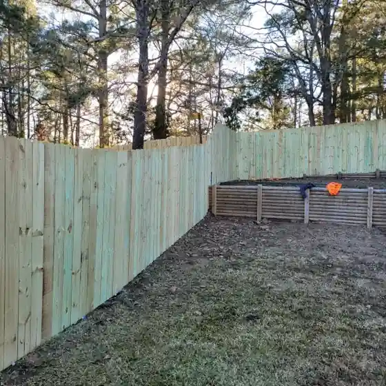 New pine privacy fence stepping down a sloped backyard behind raised garden beds